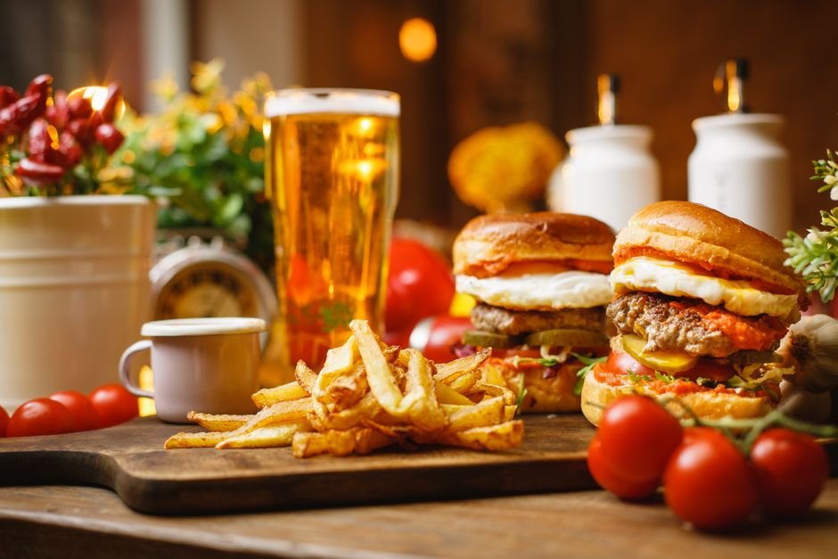 Close-up of gourmet burgers, crispy fries, and a pint of craft beer on a rustic table setting.