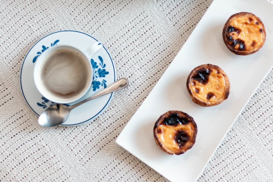 Top view of a cup of coffee with three custard tarts on a lace tablecloth.