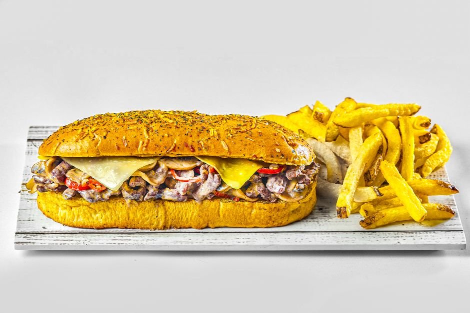 A delicious cheesesteak sandwich served with crispy seasoned fries on a white wooden board.